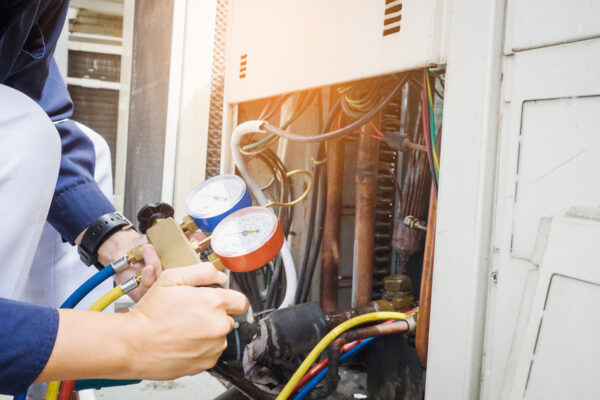 technician looking at manometer while checking pressure on outdoor air conditioning unit