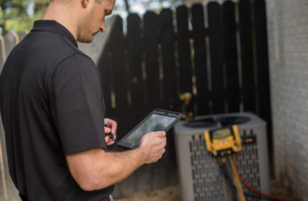 hvac technician looking at digital reader attached to outdoor hvac unit during maintenance check